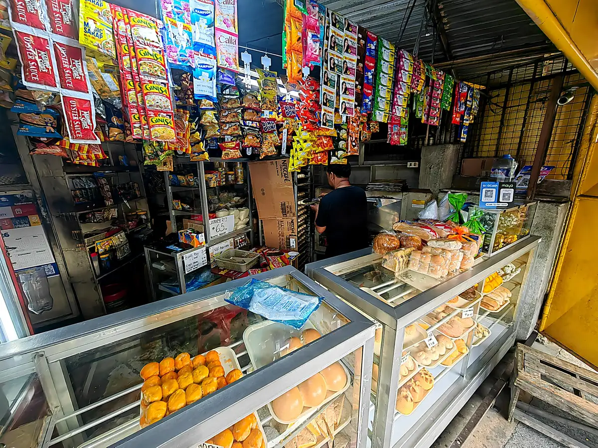 A neighborhood bakery and sari-sari store in the Philippines, with bread in glass cases and snacks hanging from the ceiling.